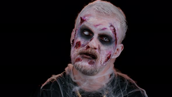 Sinister Man with Horrible Scary Halloween Zombie Makeup in Convulsions Making Faces Trying to Scare