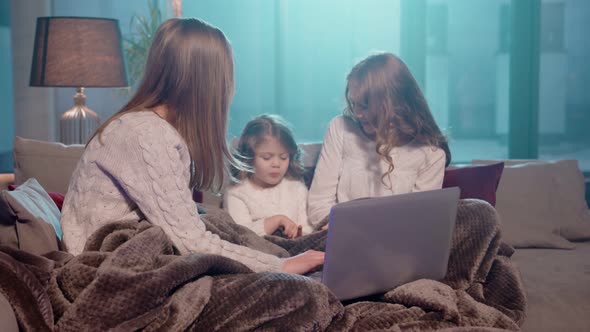 Two Girls Sitting on Couch with Mother and Using Laptop