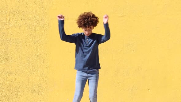 Ethnic boy with curly hair dancing on yellow wall