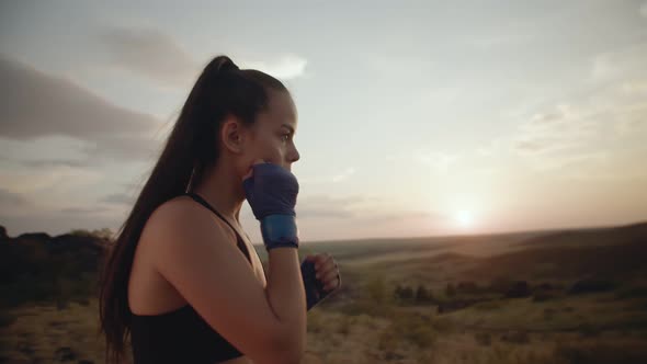 Young Woman with Bandages on Her Hands is Boxing Air in Nature Against the Background of Sunset Side