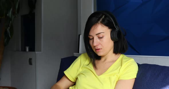 Woman in casual clothes put on headphones and click on smartphone, listening to podcast