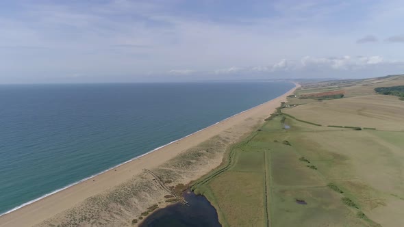 Aerial tracking forward high above Chesil Beach at Abbotsbury looking along the coastline to the wes