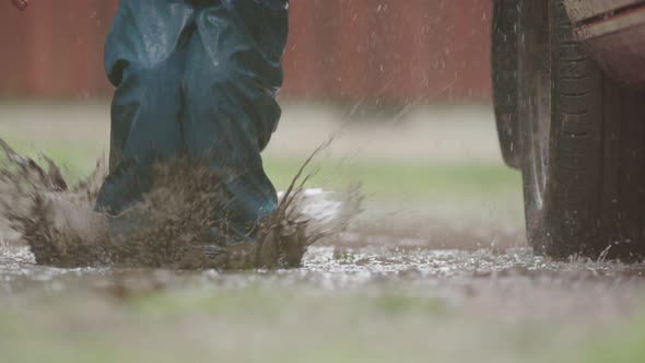 SLOW MOTION - A child jumps in a muddy puddle next to a car