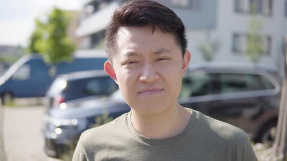 A Young Asian Man Looks at the Camera and Eventually Says Something  a Suburban Street with Cars