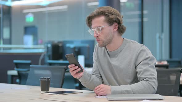 Young Businessman Celebrating Success on Smartphone in Office