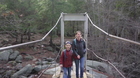 Mother and son walking over an old swinging cable bridge in the forest
