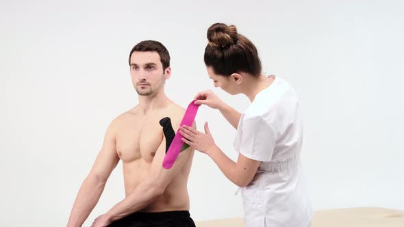 The doctor glues a special treatment tape to mail shoulder. Physiotherapist sticks kinesio tapes 