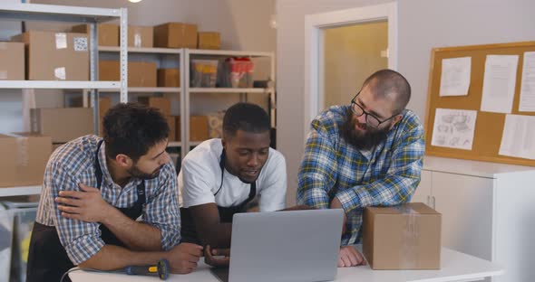 Diverse Small Business Owners Discuss Idea on Laptop in Warehouse