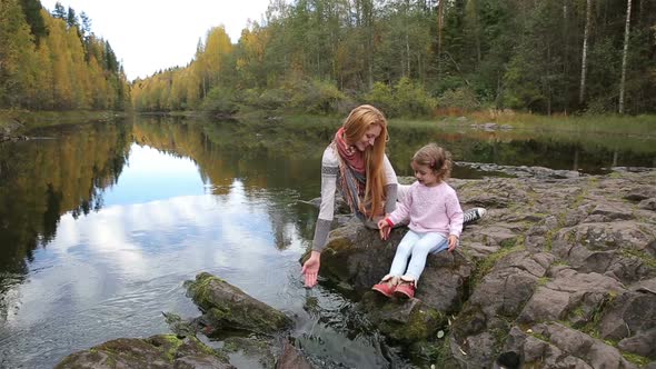 A Young Mother and Her Cute Daughter Sitting Near the Forest Stream