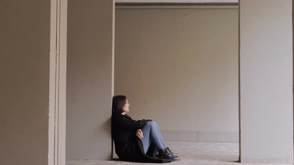 young thoughtful woman sitting on the floor with her back against the wall