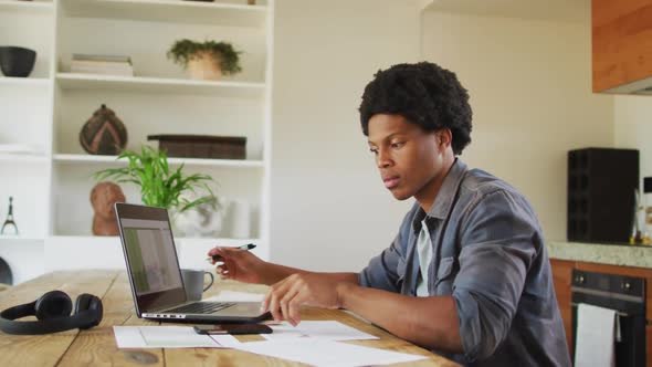 African american man working from home and using laptop and smartphone