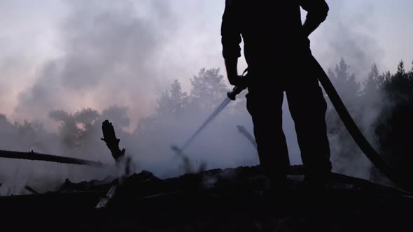 Extinguish Fire with Water By Firehose. Firefighter Hold Hose and Put Out Forest Campfire at Evening