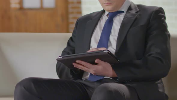 Relaxed Businessman Sitting on Couch with Tablet and Typing, Break at Lunch Time