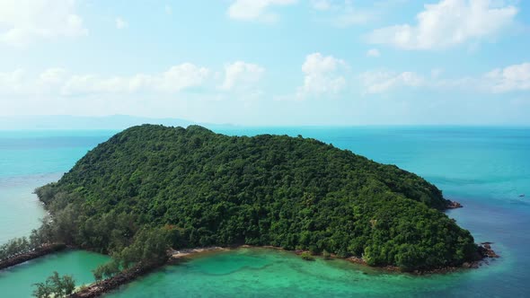 Isolated tropical island with trees forest and rocky shoreline in the middle of colorful lagoon with