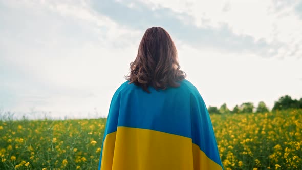 Unrecognizable Ukrainian Patriot Woman Standing with National Flag in Canola Yellow Field