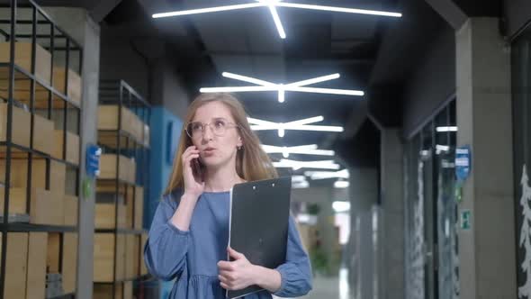 businesswoman with smartphone and documents walks down corridor of office