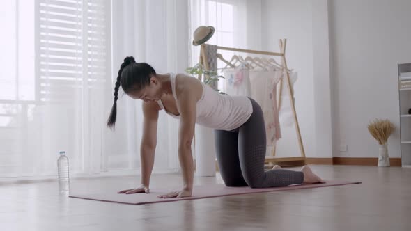 Asian woman practicing yoga pose Cat and Cow at home.