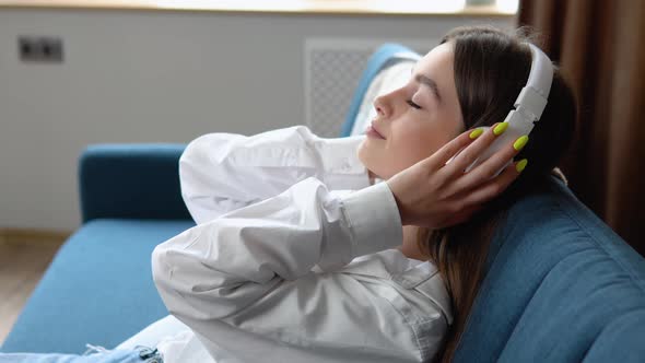 Woman Listening Music in Headphones While Sitting on Sofa in Room