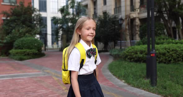 Happy Little Caucasian Blonde Girl Seven Years Old in Uniform with Yellow Backpack Going Back to