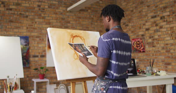 African american male painter painting from photograph on canvas in artist studio