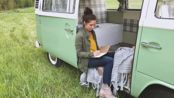 Woman sitting in camper and writing in daybook