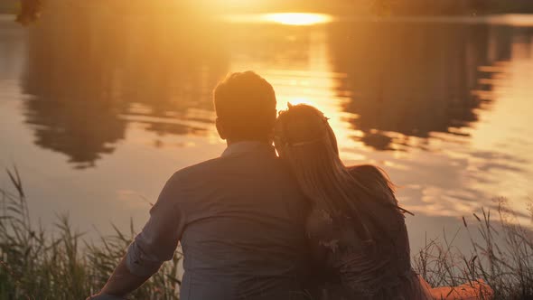 A Young Couple Sits on a Lake at Sunset