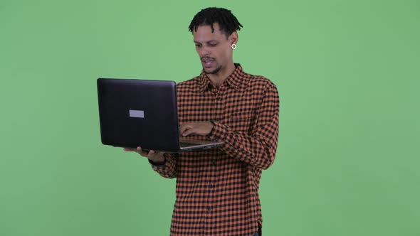 Happy Young Handsome African Man Talking While Using Laptop