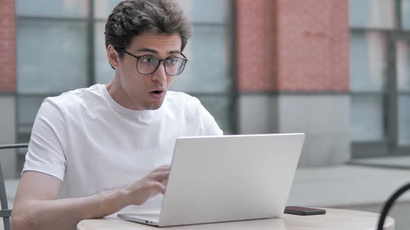 Young Man Shocked by Results on Laptop, Sitting Outdoor