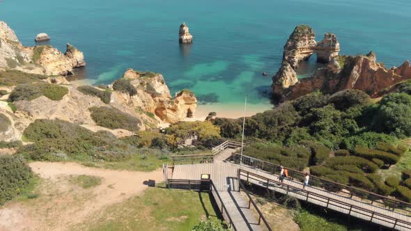 Reveal of Camilo Beach over steep hill with a wooden walkway, Lagos, Algarve, Portugal