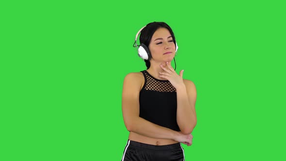 Young Sporty Beautiful Woman Enjoying the Music in Headphones on a Green Screen, Chroma Key