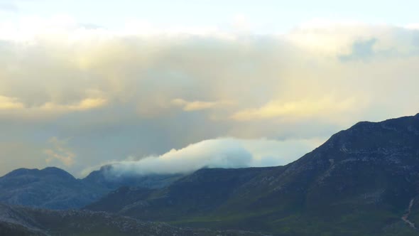 Time lapse of a mountain range with low fast moving clouds beneath high puffy clouds in the evening