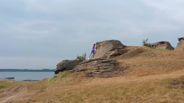 A Girl is Doing Fitness on a Hill on the Lake Shore