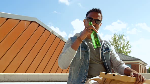 Indian Man Eating Pizza and Drinking Beer Outdoors
