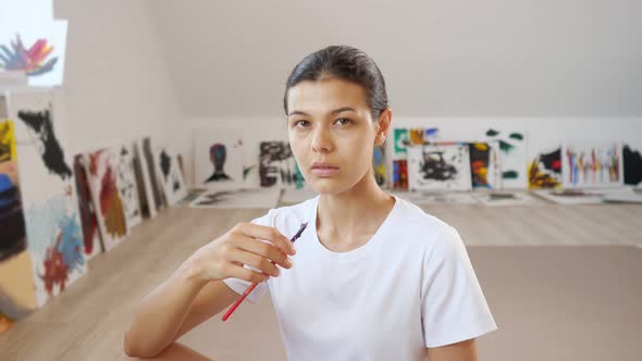 Young Woman Poses Smiling Against Own Paintings at Walls