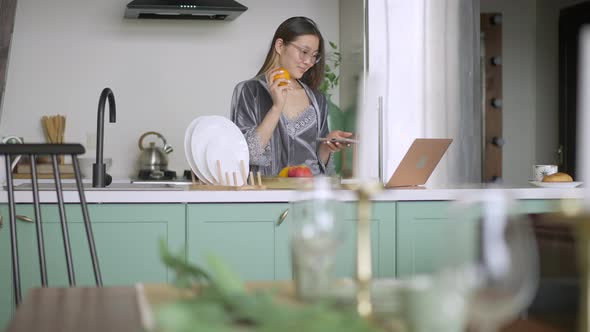 Wide Shot of Happy Young Woman Standing in Kitchen in the Morning Messaging Online in Video Chat