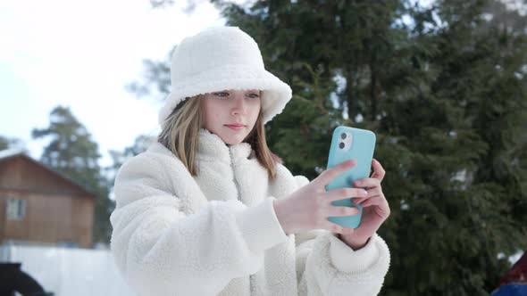Focused Young Girl in Stylish Outfit Using Smartphone Outdoors at Wintertime