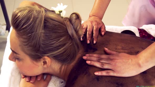 Relaxed Woman Lying on Spa Bed for Body Scrubbing Massage Using Traditional Herb