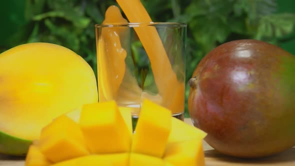 Mango Juice is Poured in a Glass on the Background of Greenery