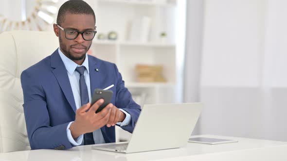 Focused African Businessman Using Laptop and Smartphone in Office 