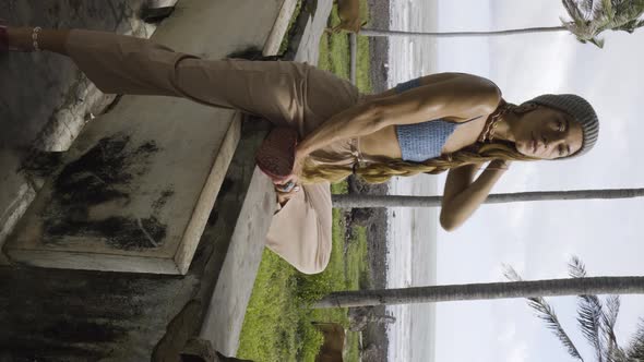 Vertical gimbal shot of woman sitting on wall of abandoned house near beach