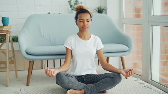 Pretty Mixed Race Girl Is Sitting on Floor in Lotus Position with Hands on Knees and Meditating