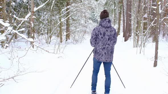 Skier in hat with pompom with ski poles in his hands with in snowy forest with snow