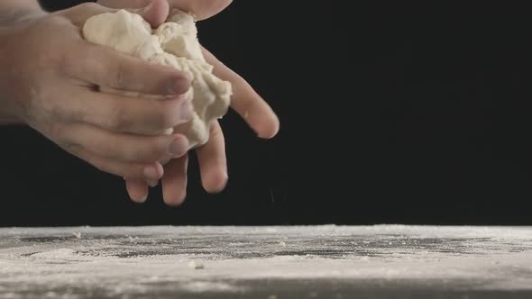 Male Hands Knead a Piece of Dough and Tears It in Half Above Wooden Table Sprinkled with Flour