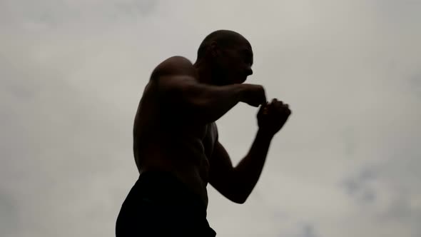 a Male Silhouette with a Bare Torso is Boxing Against a Light Sky Background