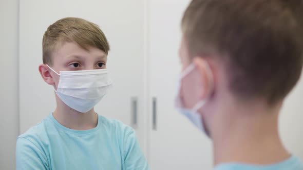 A Young Boy Adjusts His Face Mask in Front of a Mirror in an Apartment - Closeup