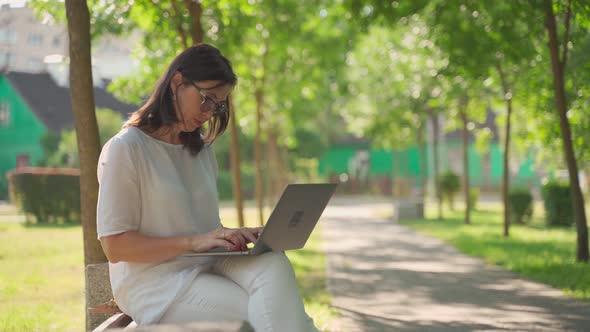 Joyful Adorable Beautiful Business Senior Woman Wearing Eyeglasses Sittingin Park Outdoors, Working