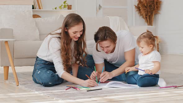 Happy Family Home Leisure Young Parents Drawing Coloring Picture with Pencils Laying on Floor