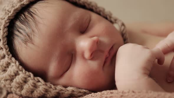 Newborn baby sleeping peacefully with checkered cloth on brown background.