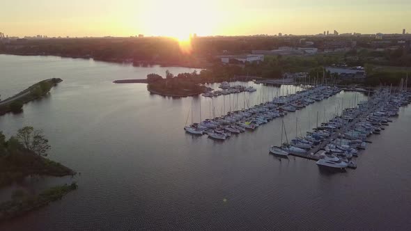 Aerial Sunset Wide Shot Sliding Right Toward Sailboat Marina Yacht Club Dock In Lake Bay Among Green