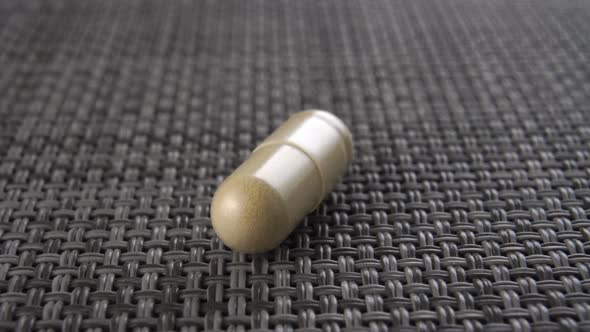 Herbal alternative medicine capsule close-up on a gray plastic surface